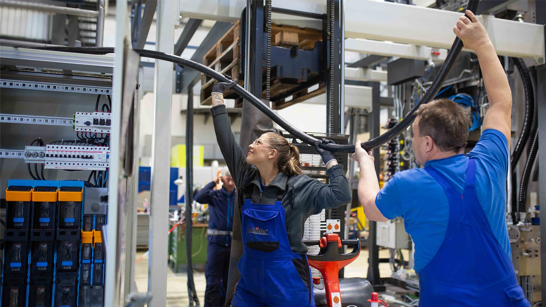 Eine junge Frau und ein männlicher Kollege helfen sich gegenseitig beim Heben eines schweren Kabels. 
