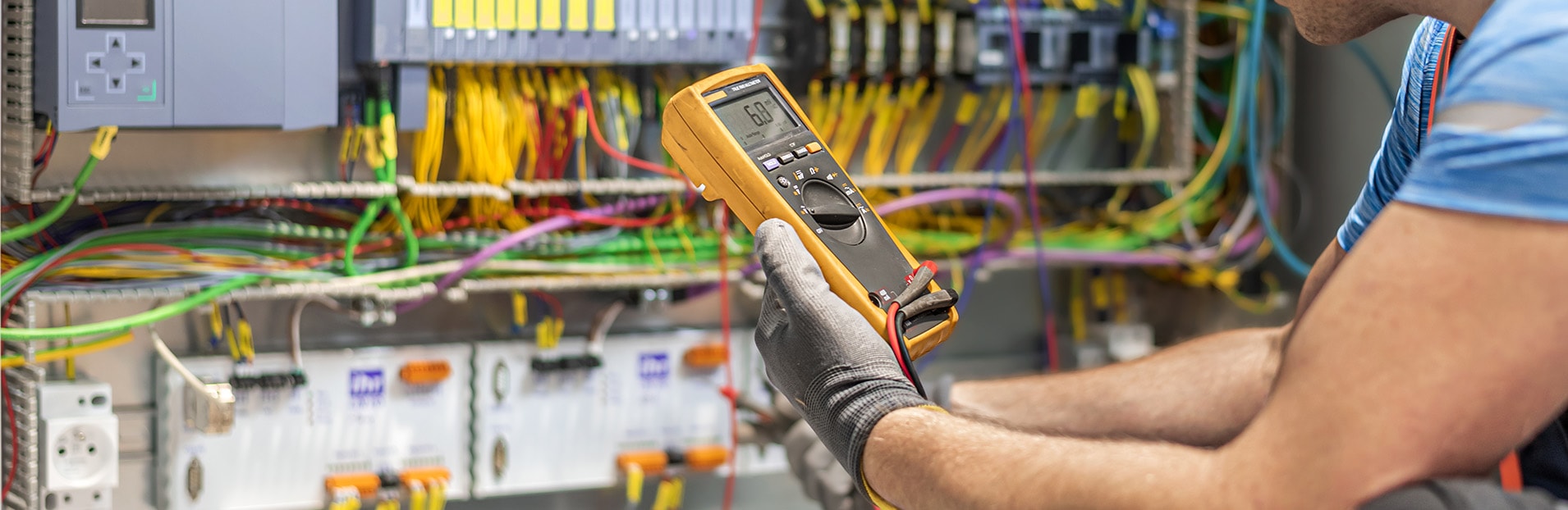 Mann prüft mit einem Multimeter eine elektrotechnische Anlage.