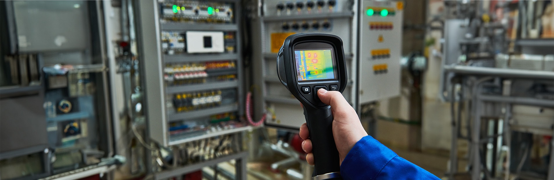 Eine Person prüft eine elektrotechnische Anlage mithilfe einer Wärmebildkamera.