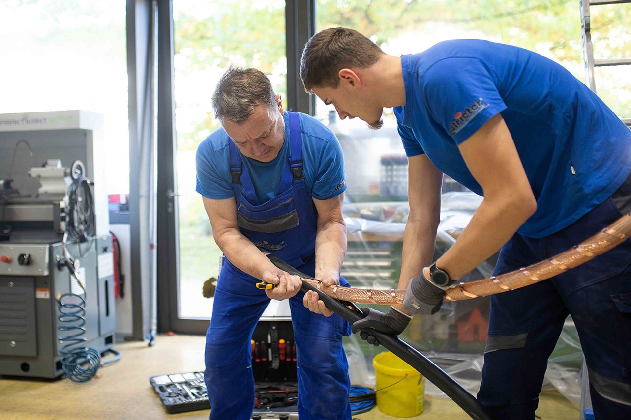 Zwei männliche Arbeitskollegen arbeiten gemeinsam an einem schweren Kabel für den Netzausbau.
