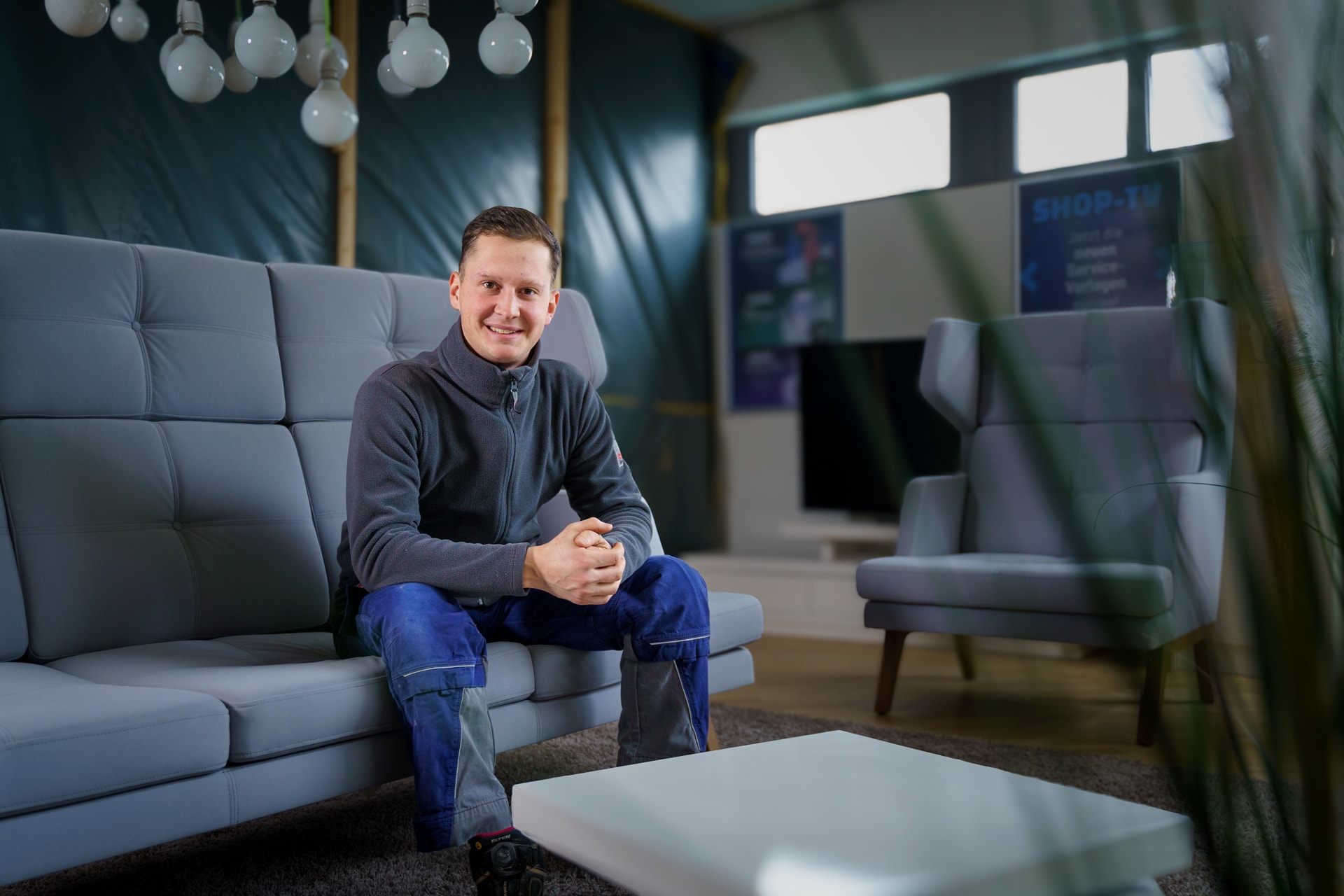 Niklas Bär, Mitarbeiter im Bereich Netzbau, sitzt auf einem Sofa und lächelt in die Kamera